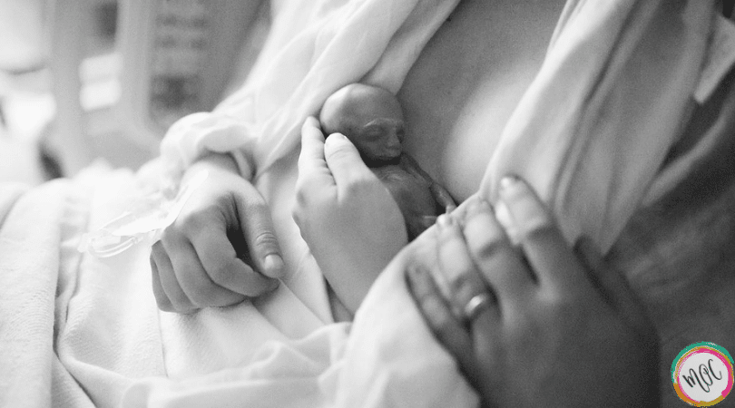 Holding my baby after inducing at 19.5 weeks. April Rey had trisomy 13. This picture shows her wrapped in a blanket, doing skin to skin on my chest. My husband's hand is resting on my arm as I cradle my dying child.