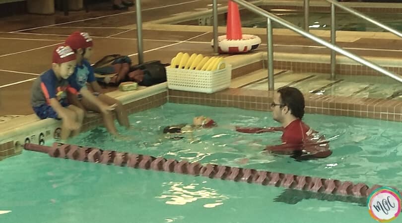 British swim school turtle level 1, girl in red swim cap doing back stroke to her instructor.