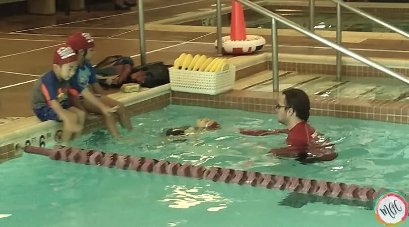 British swim school turtle level 1, girl in red swim cap doing back stroke to her instructor.