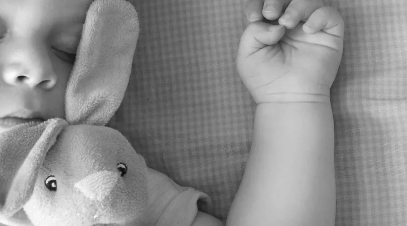 Baby sleeping with arm up next to stuffed bunny. This baby is extra tired and taking a long nap, so flexibility with babywise schedule is needed today.