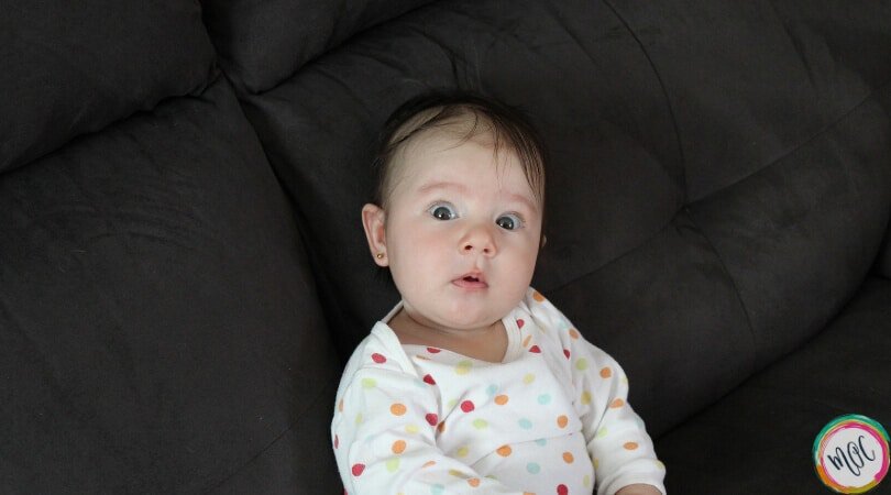 Baby sitting up on the couch wearing a polka dot long sleeve onesie. She is having wake time and it's getting to be nap time, as she uses the eat wake sleep cycle.