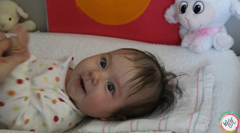 Baby lying on changing table with polka dot onesie on smiling. Just woke up from nap and is being changed. Will eat next as a part of the eat wake sleep cycle.